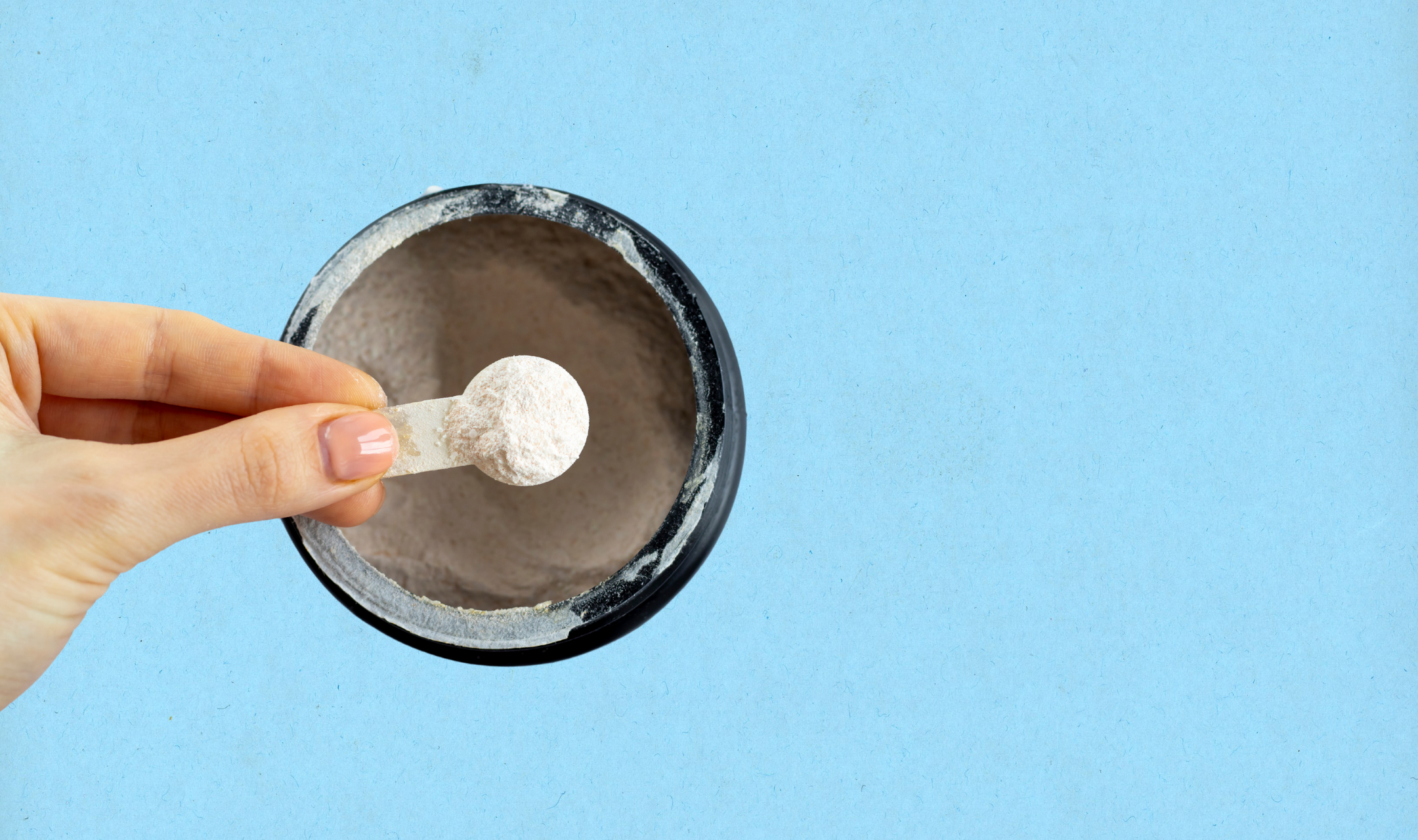 Hand holding a small scoop of white powder above an open black container, set against a light blue background. The scene conveys a clean and organized feel.