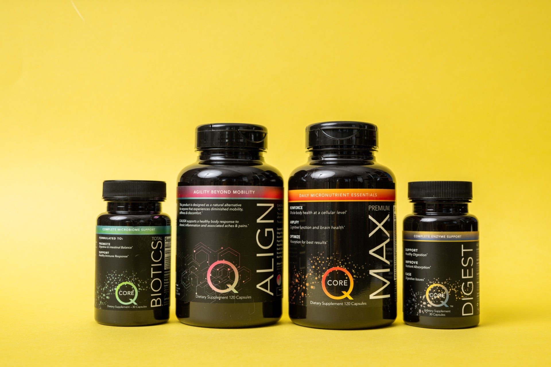 Four dietary supplement bottles with black labels and colorful accents are lined up against a vibrant yellow background. Each bottle varies in size.